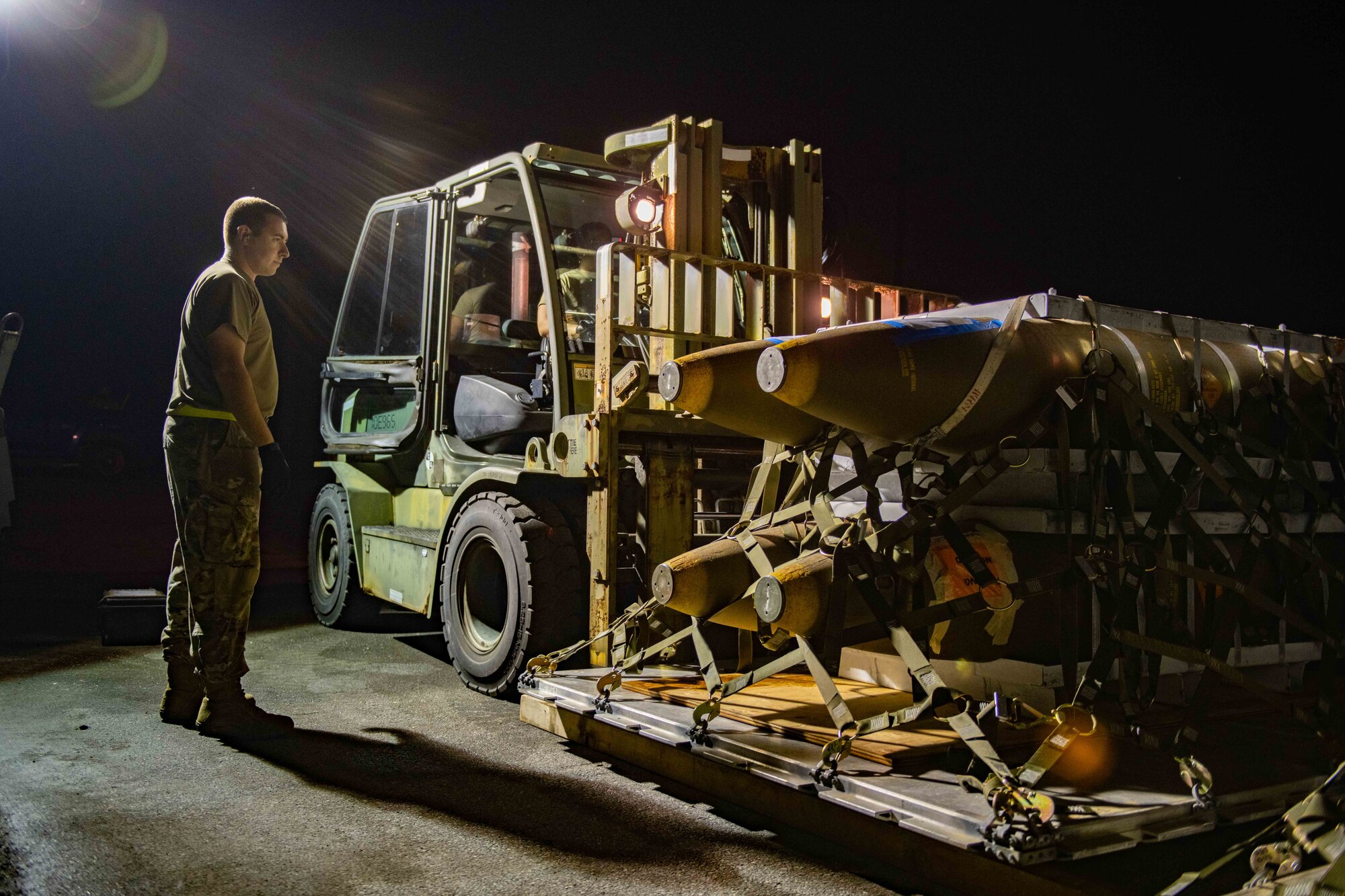 An Airman guides a forklift operator as he picks up a pallet of munitions