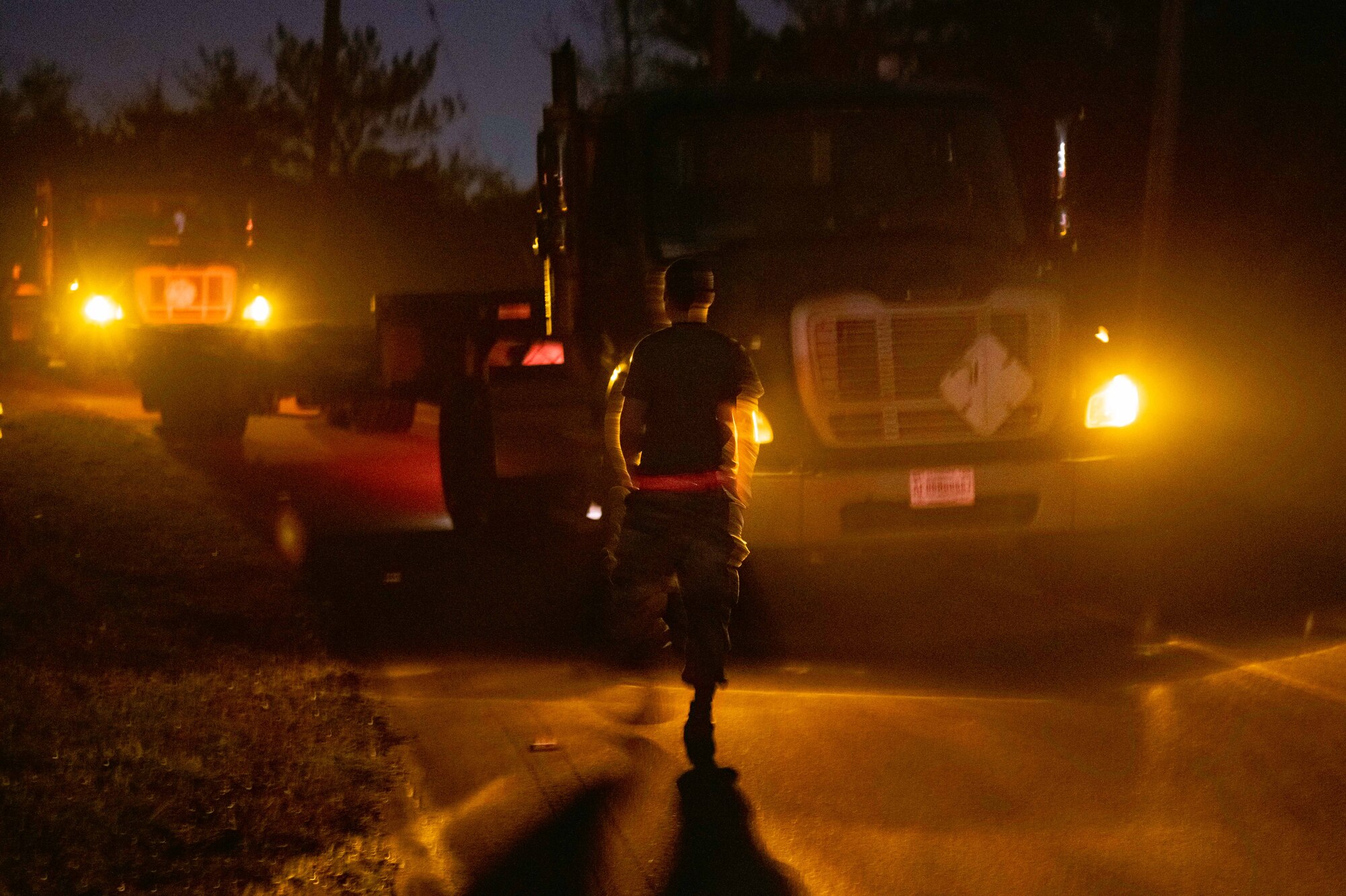 An Airman walks toward two trucks in the night