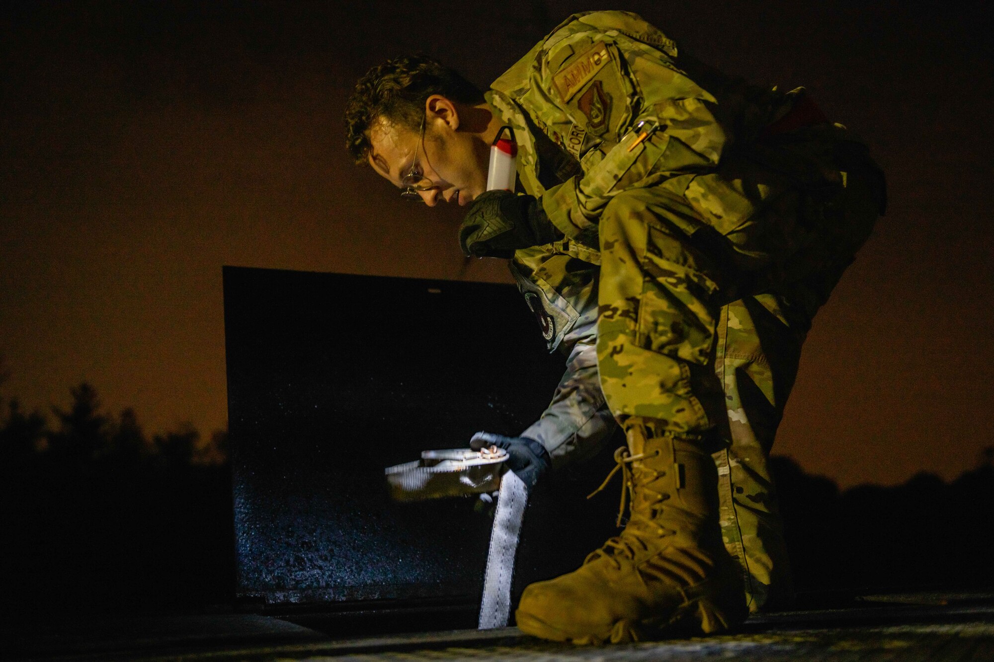 An airman pulls out a rope used to secure pallets of munitions to the back of a truck at night