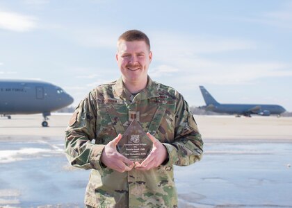 Capt. Lambert stands on flight line holding the award with two planes in the background.