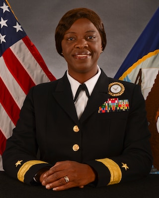 Offical portrait of woman in her uniform smiling at camera with USA and Navy flags in background