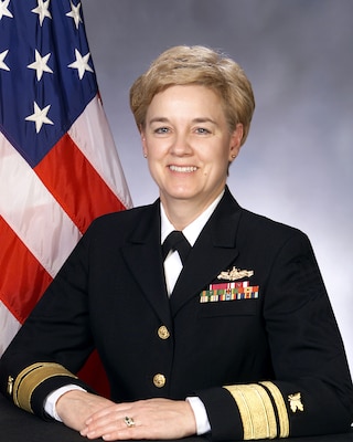 Official portrait photo of woman in her uniform smiling at camera with USA flag in background