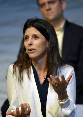 Woman in her white blazer and black top, speaking at conference