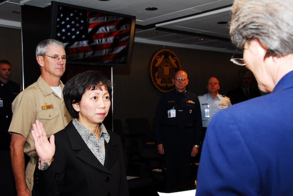 Ms. Giao L. Phan, woman in her civilian attire with her hand up being sworn with people behind her watching
