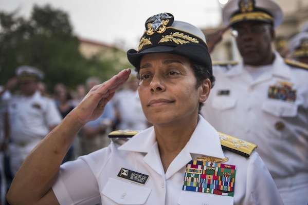 Woman in her white uniform saluting with sailors behind her