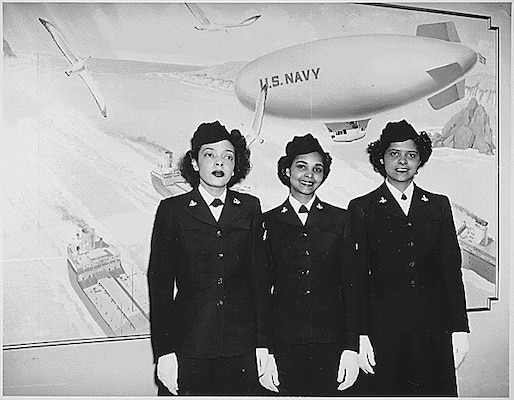 Black and white photo of 3 black women in their uniform smiling at camera with navy blimp painting in background