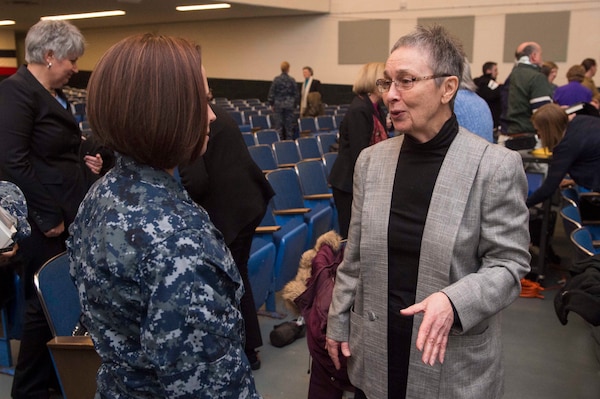 Woman in her grey blazer and black top, speaking with sailor in her blue uniform