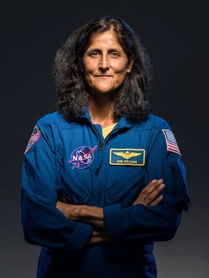 Official portrait of woman in her astronaut uniform smiling at the camera crossing her arms