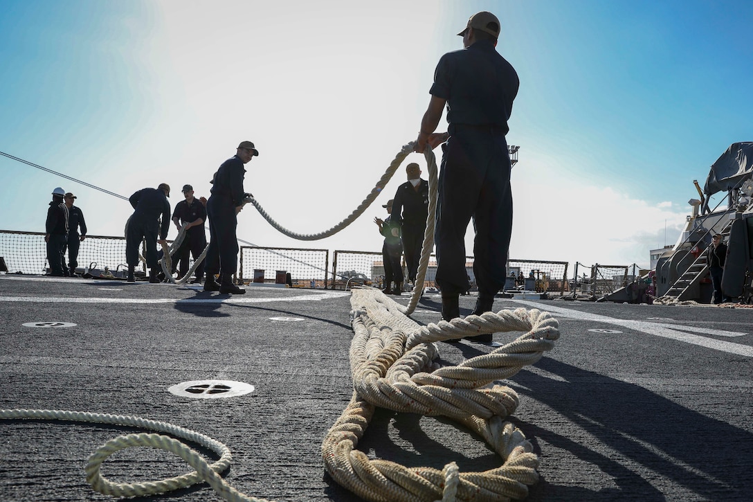 Sailors handle a mooring line aboard a ship.