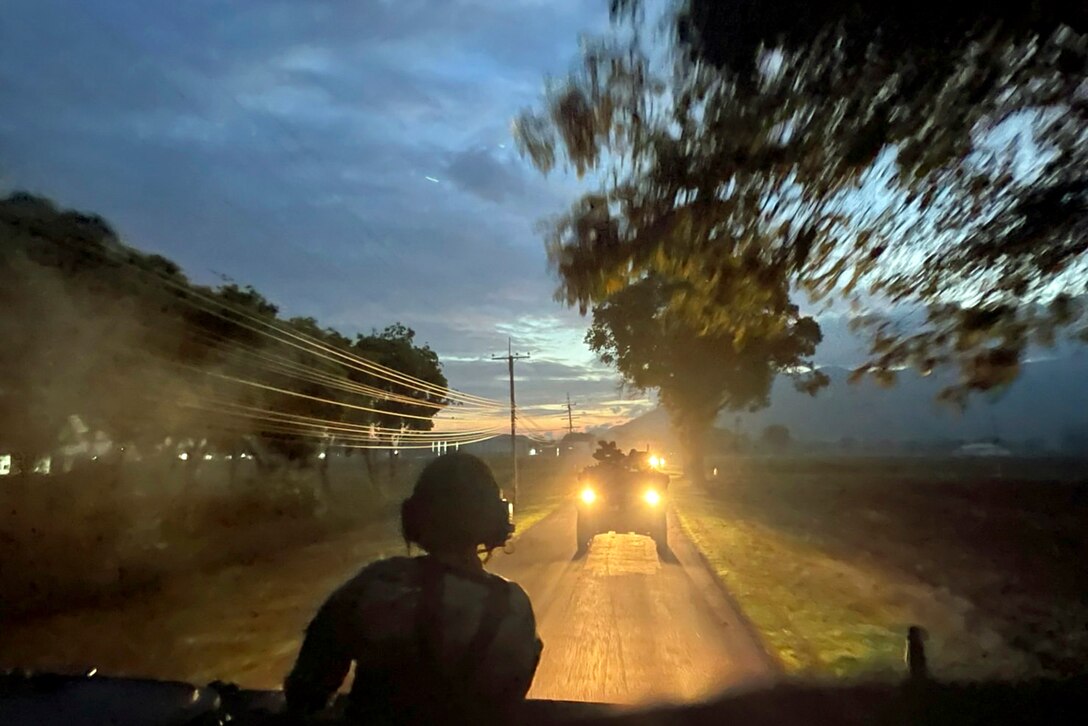 Soldiers ride in large vehicles at night.
