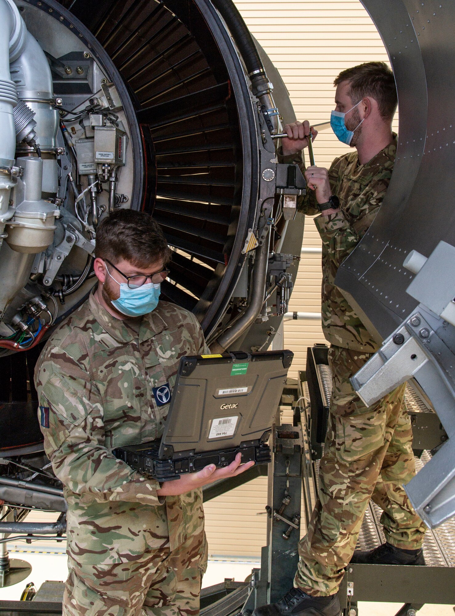 Royal Air Force Senior Aircraftman Technician Joseph Eastham, reads technical orders from a laptop as RAF Cpl. Ben Archer removes a bolt from a C-17 engine trainer at Dover Air Force Base, Delaware, Feb. 15, 2022. Eastham and Archer, both C-17 Globemaster maintainers from 99 Squadron, RAF Brize Norton, United Kingdom, attended the 64-hour C-17 Engine Change course where they learned how to safely remove and reinstall the Pratt & Whitney F117-PW-100 turbofan engine. (U.S. Air Force photo by Roland Balik)