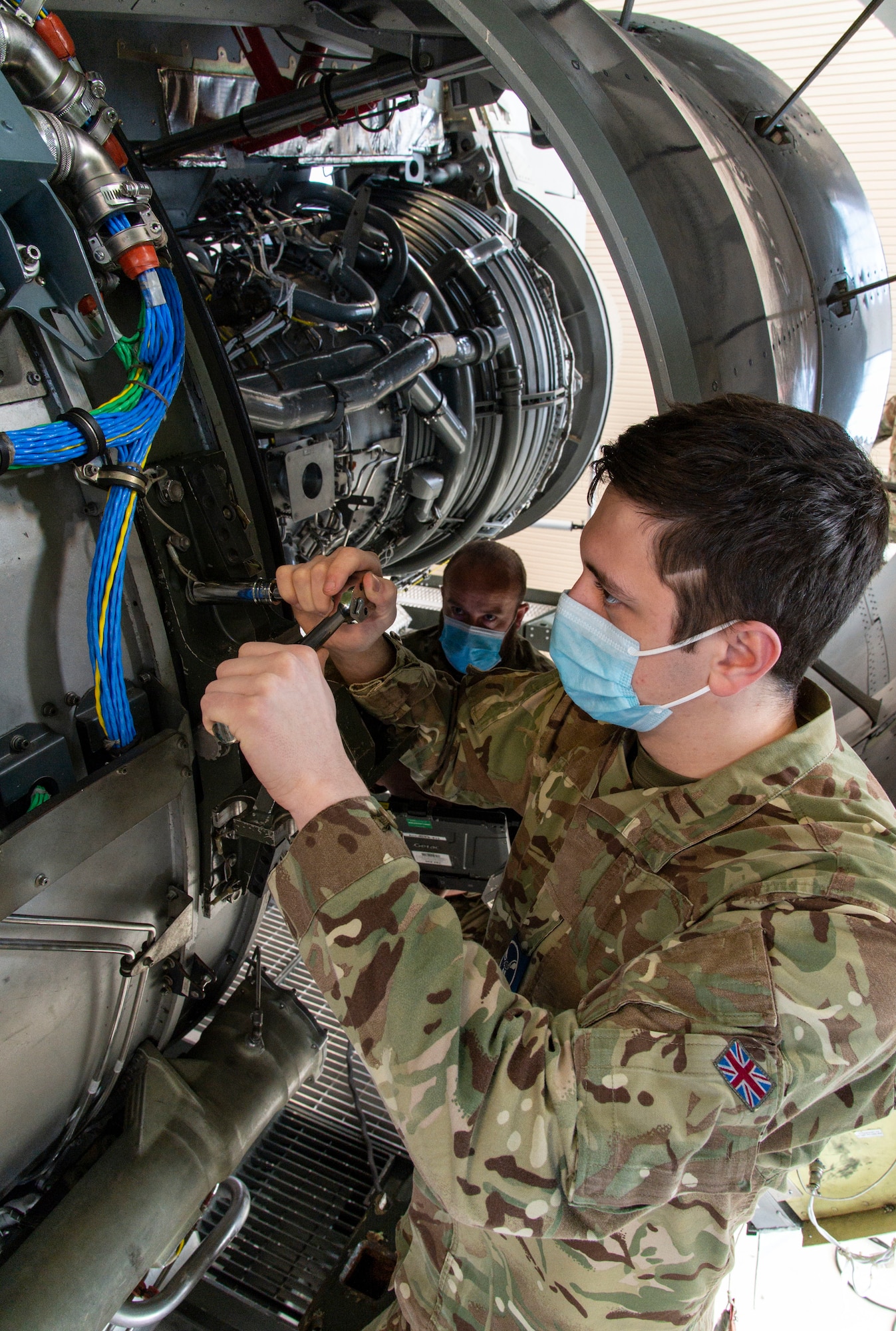 Royal Air Force Senior Aircraftman Technician William King removes a bolt from a C-17 engine trainer as RAF Sgt. David Stephens reads technical orders from a laptop at Dover Air Force Base, Delaware, Feb. 15, 2022. King and Stephen, both C-17 Globemaster maintainers from 99 Squadron, Royal Air Force Brize Norton, United Kingdom, attended the 64-hour C-17 Engine Change course where they learned how to safely remove and reinstall the Pratt & Whitney F117-PW-100 turbofan engine. (U.S. Air Force photo by Roland Balik)