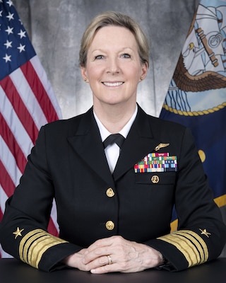 Official portrait photo of woman in her uniform with USA and Navy flags in background