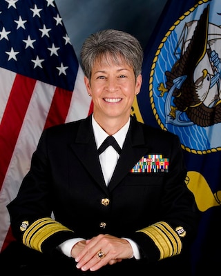 Official portrait photo of woman in her uniform with USA and Navy flags in background