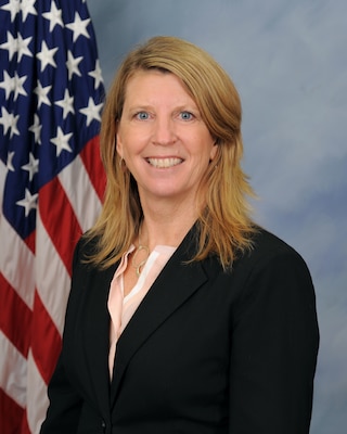 Offical portrait photo of smiling woman in her suit with USA flag in background