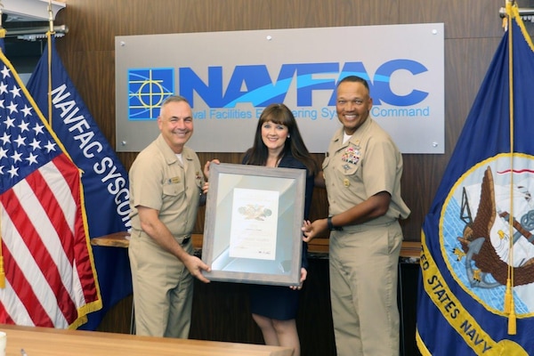 Woman in her suit holding award with rear admiral and master chief