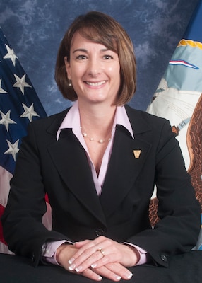 Official portrait photo of smiling woman in her suit with USA and navy flag in background