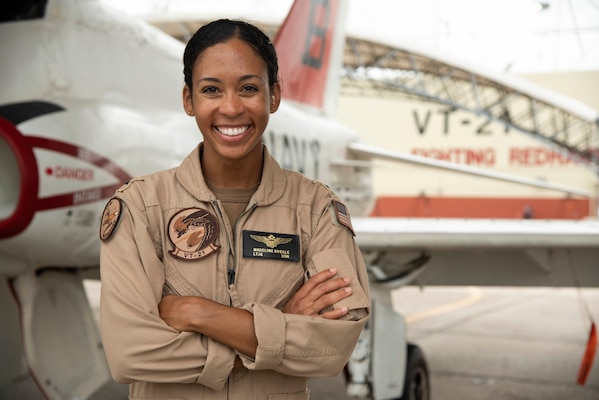 Woman smiling in beige aviator uniform standing front of aircraft