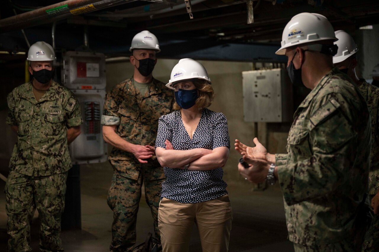 A woman and four men wear hard hats inside a facility.