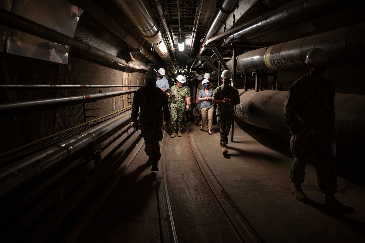 People wearing hard hands walk in a confined space underground.