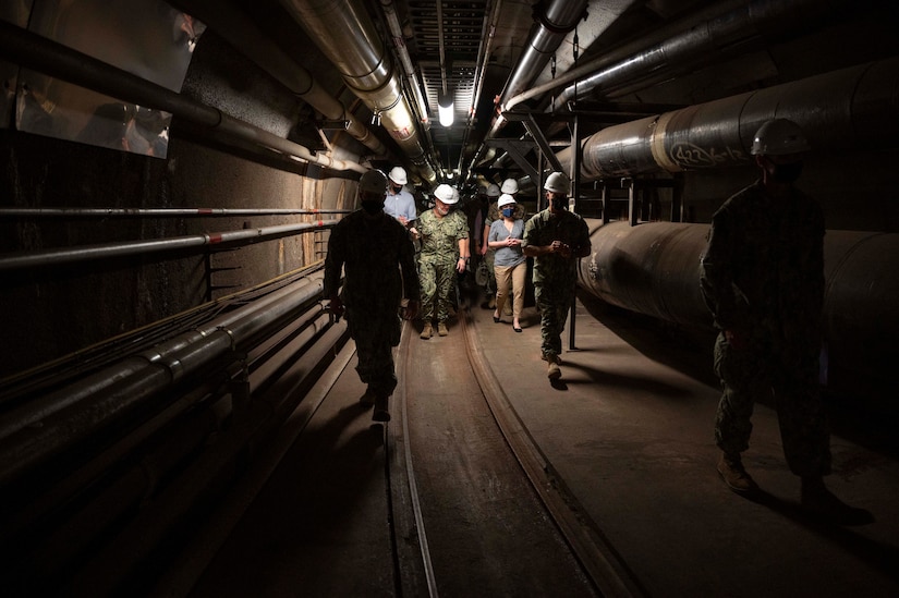 People wearing hard hands walk in a confined space underground.