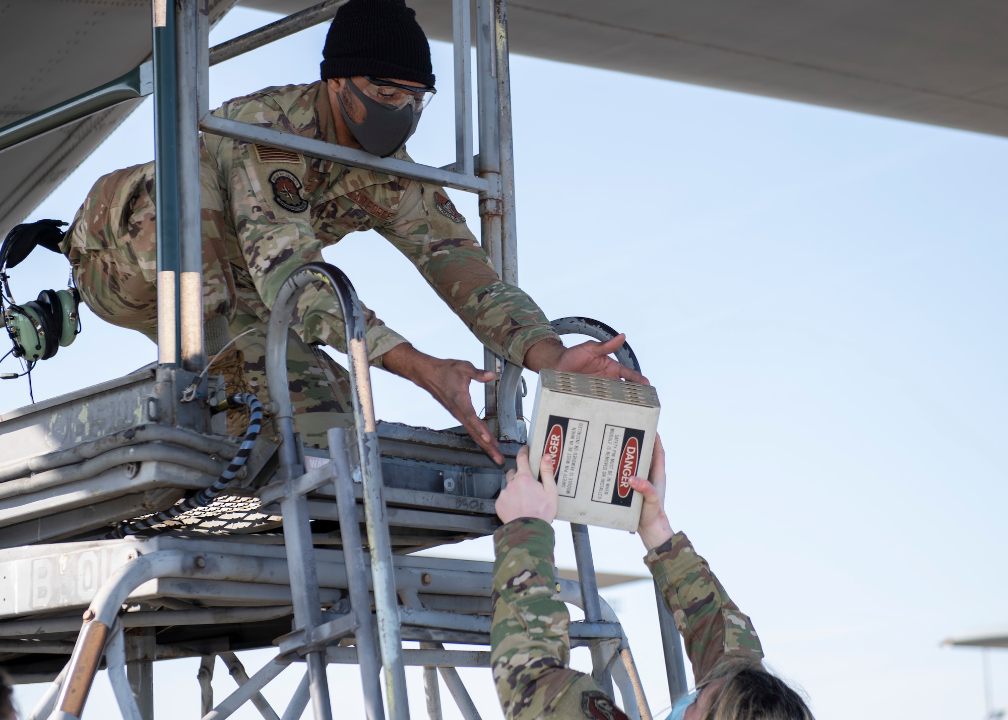 One airman hands a chaff cartridge to another atop a lift.