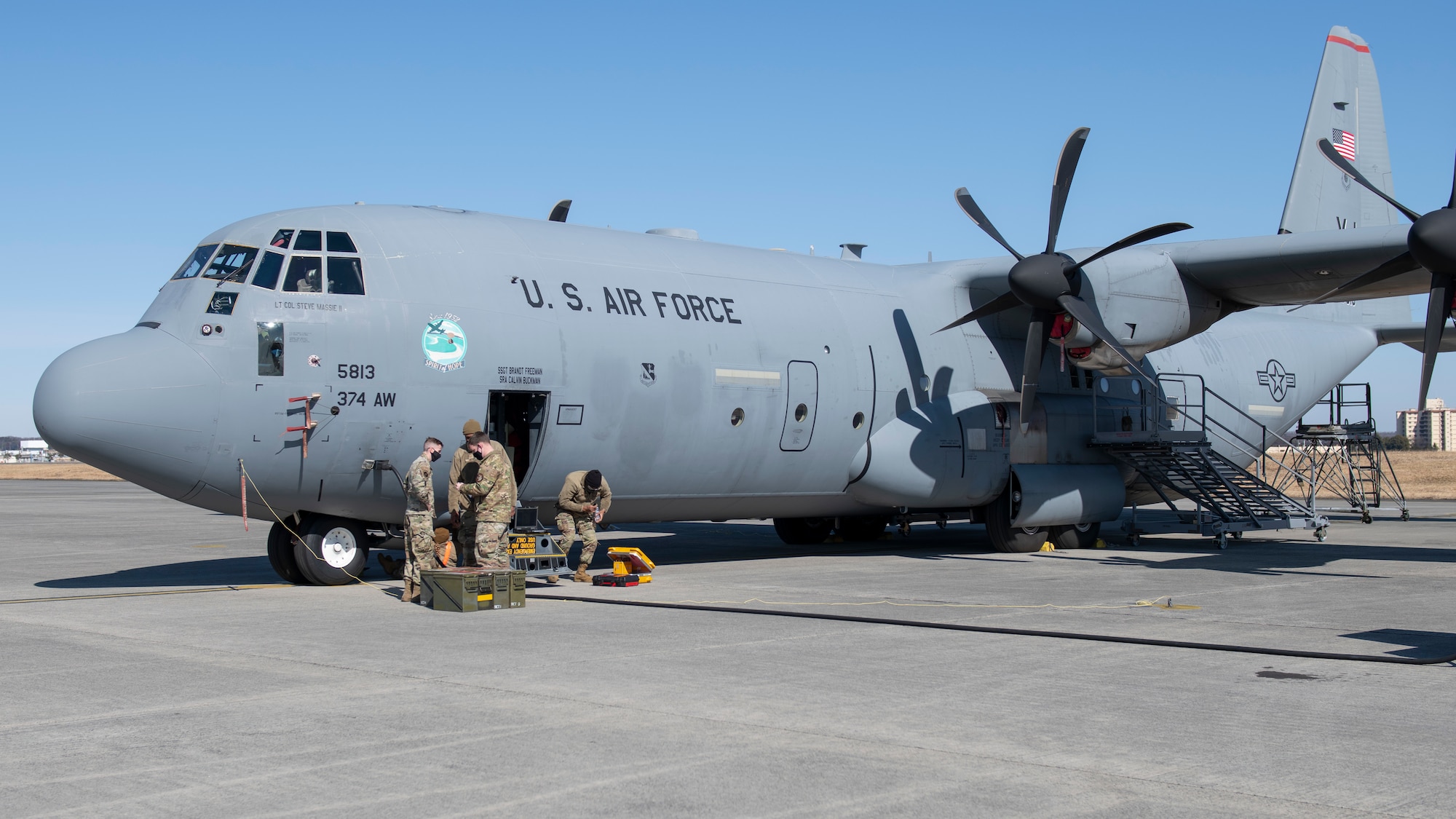 Maintenance Airmen sort through supplies in front of a military cargo plane.