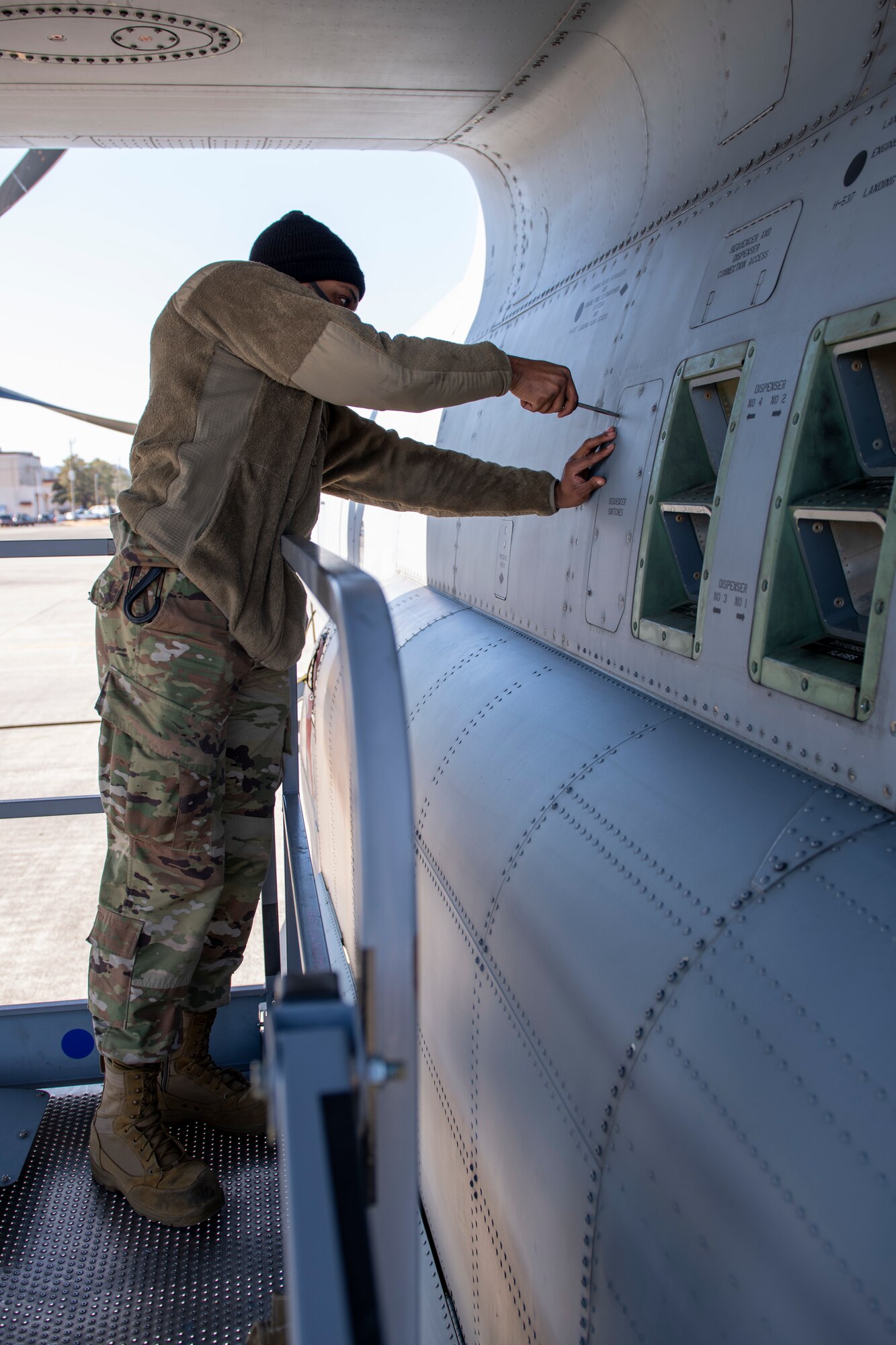 An Airman opens up munitions panels on the side of a military cargo aircraft.