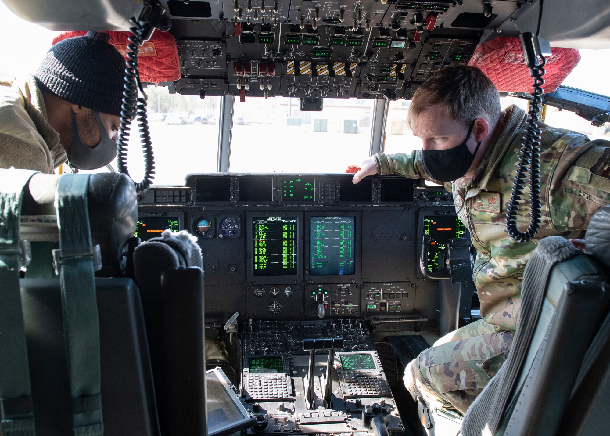 Two maintainers work the cockpit computer of a military cargo aircraft.