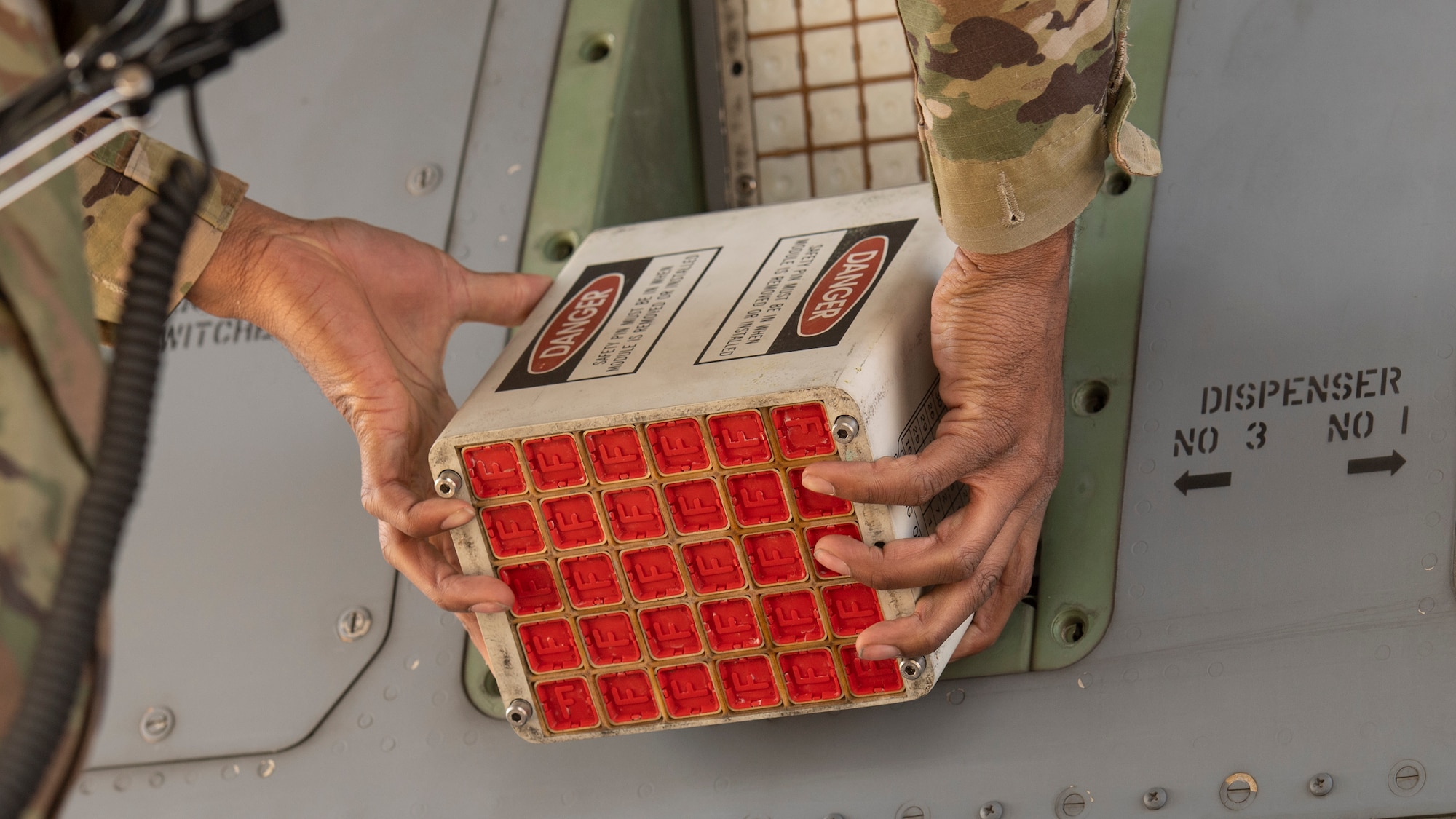 A close-up of an Airman loading a box of flares into the side of an airplane.