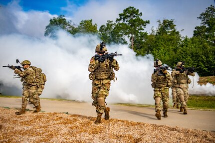 Soldiers carrying guns walk through smoke during training exercise.