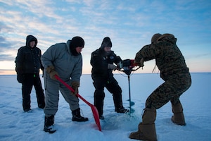Sailors, Marines and members of Arctic Submarine Laboratory carve a hole into Arctic sea ice using a six-inch auger to prepare for a submarine to breach the ice at Ice Camp Queenfish during Ice Exercise (ICEX) 2022.