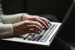 Close up of two hands typing on a laptop keyboard.