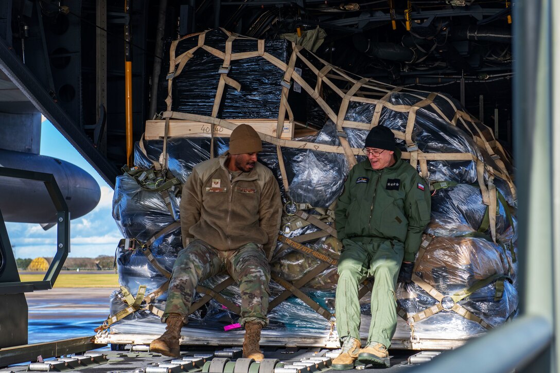 An airman and Polish officer load luggage and equipment into a KC-130 plane.