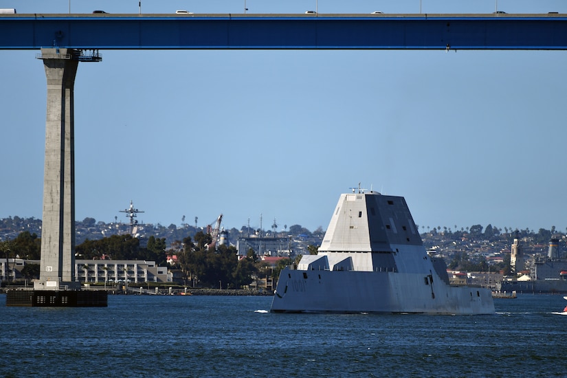 An angular ship traverses a waterway under a large bridge.