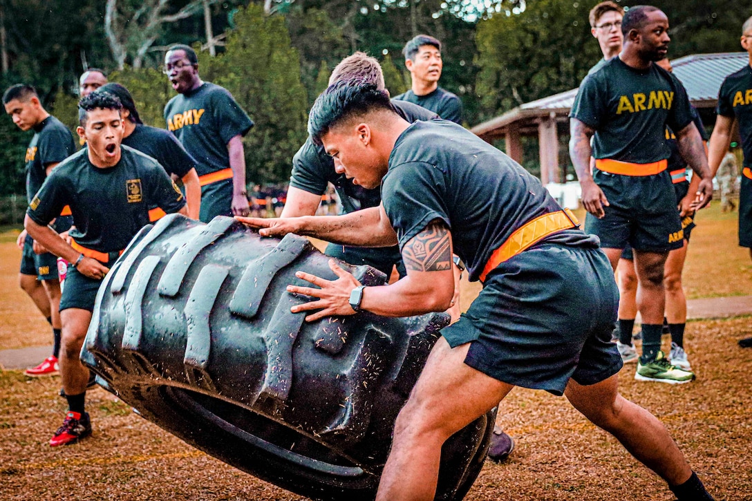 Soldiers flip a tire in a field.