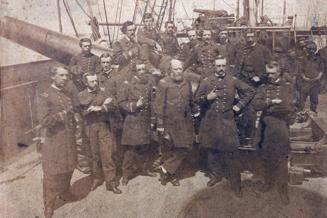 More than a dozen men in uniform pose on a ship’s deck for a photo.