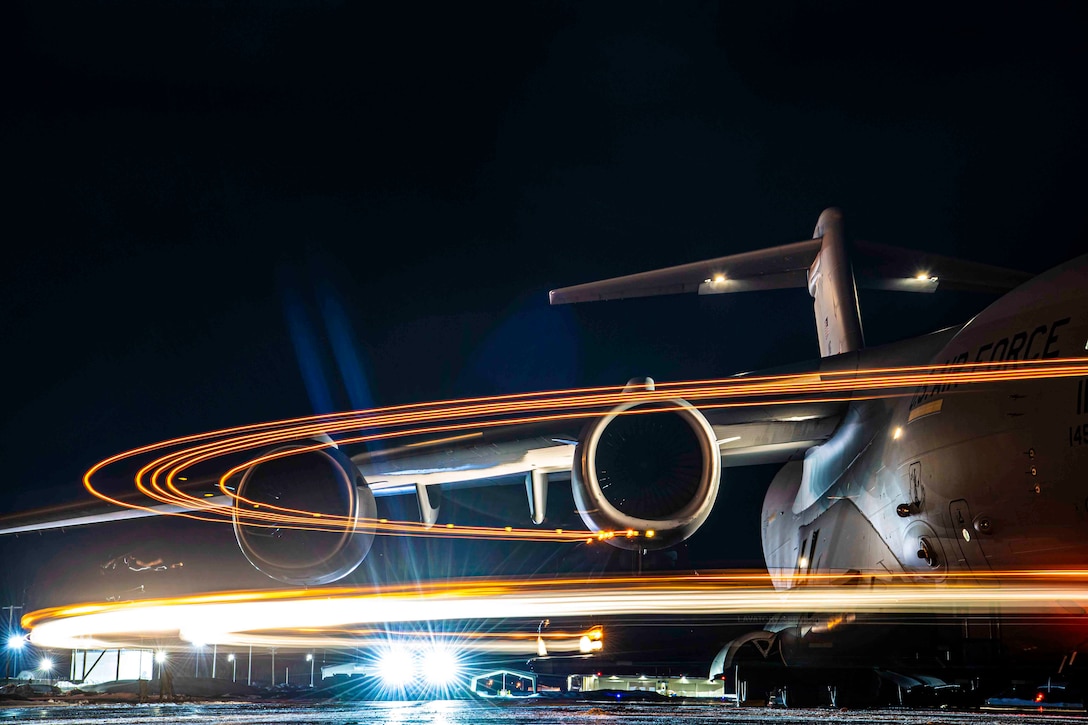 Lights shine around a parked aircraft at night.