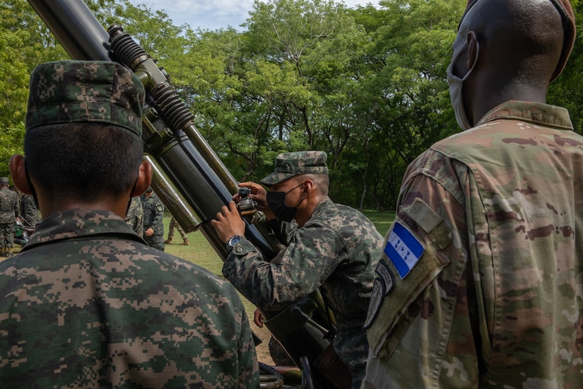 Military personnel stand around a piece of military hardware.