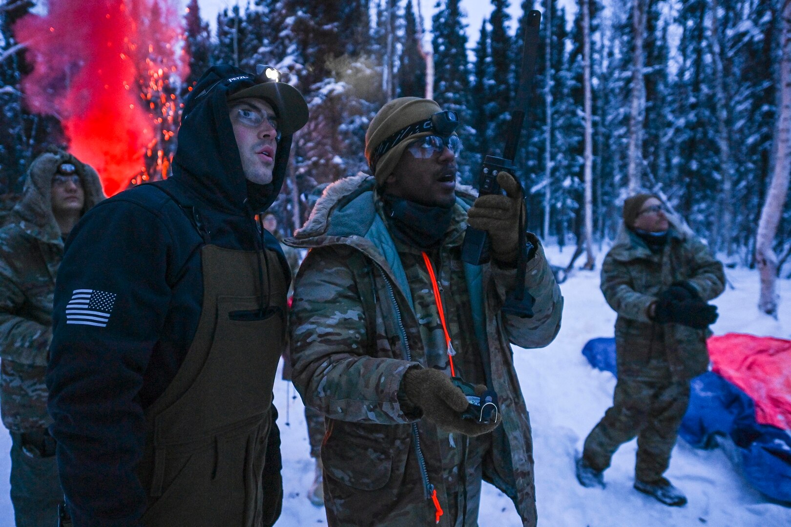 Two men stand near each other outdoors in a winter environment. One is holding a radio and a compass.
