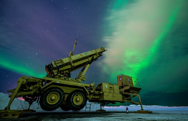A piece of military hardware sits on the snow. The sky is illuminated with greenish lights.