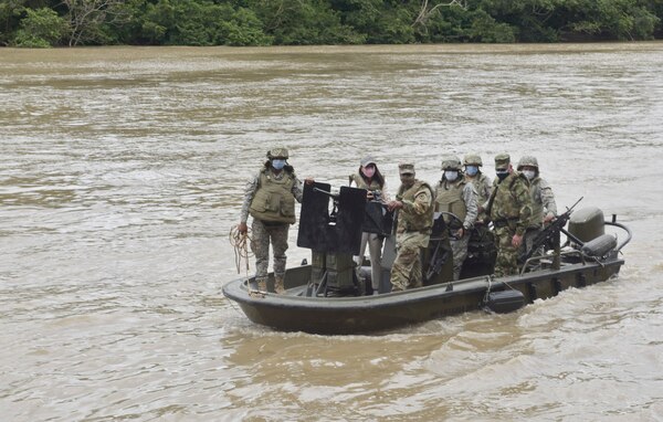 Seven military personnel ride a small boat on a waterway.