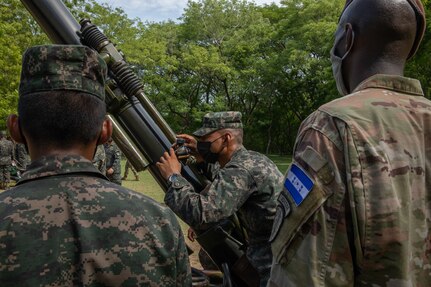 Military personnel stand around a piece of military hardware.
