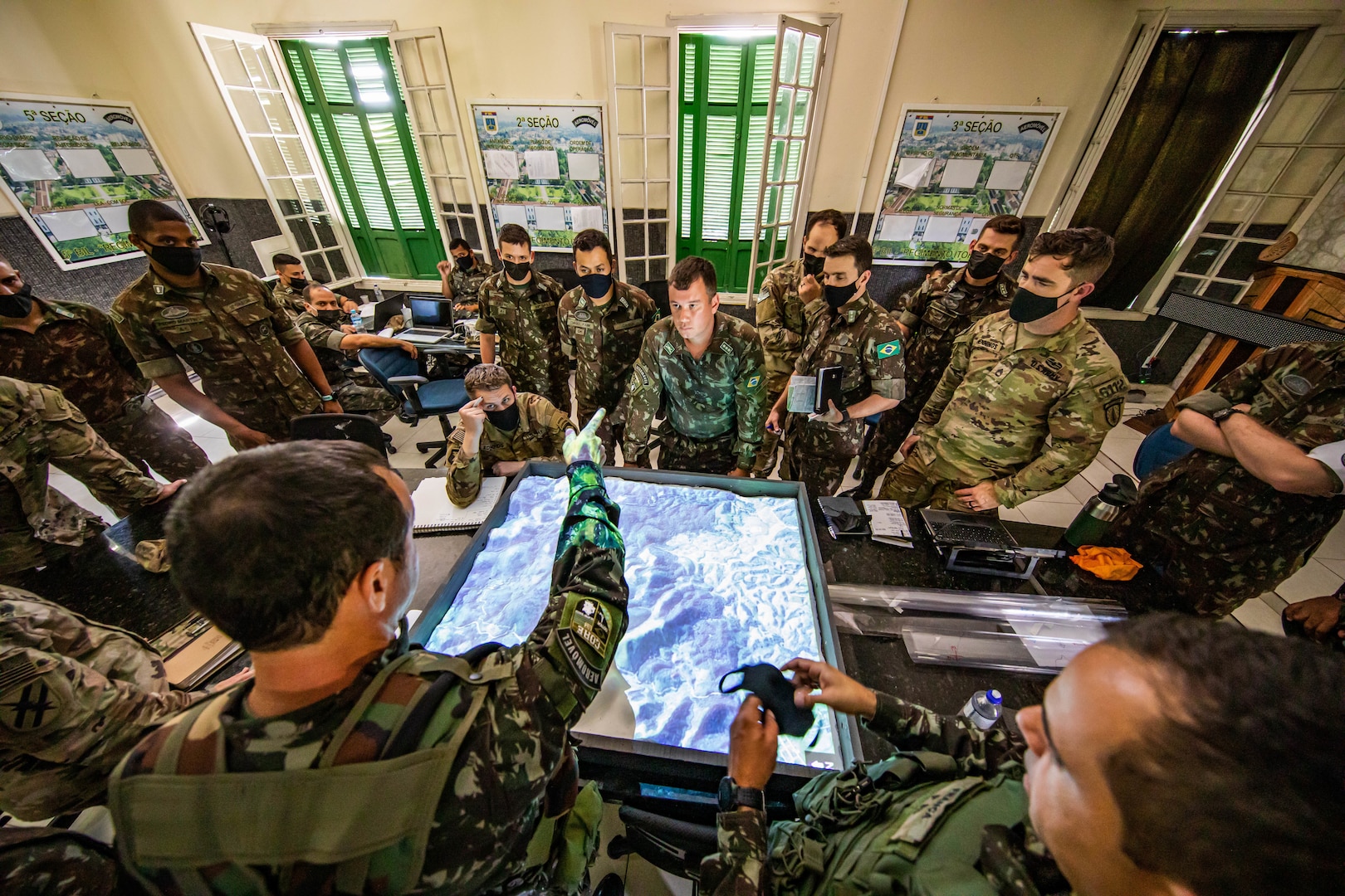 Multiple military personnel stand around a digital sand table.