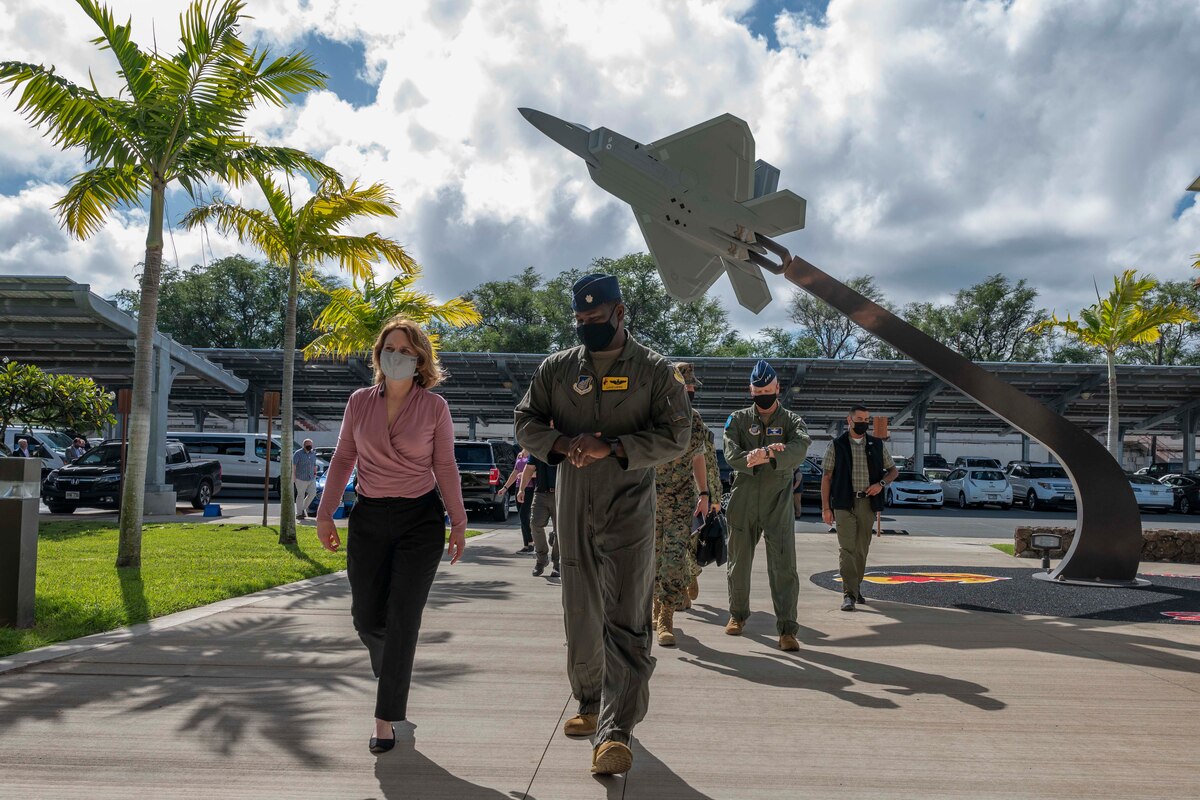 A woman walks with an Airman. A statue of a jet is to their left.