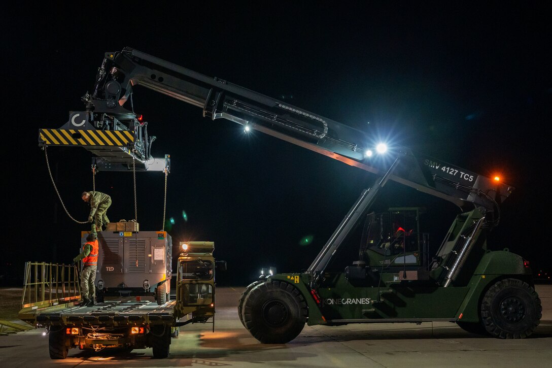 Air Force and Lithuanian personnel move an aircraft maintenance air conditioning unit with a heavy-lift crane.