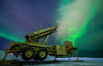A piece of military hardware sits on the snow. The sky is illuminated with greenish lights.