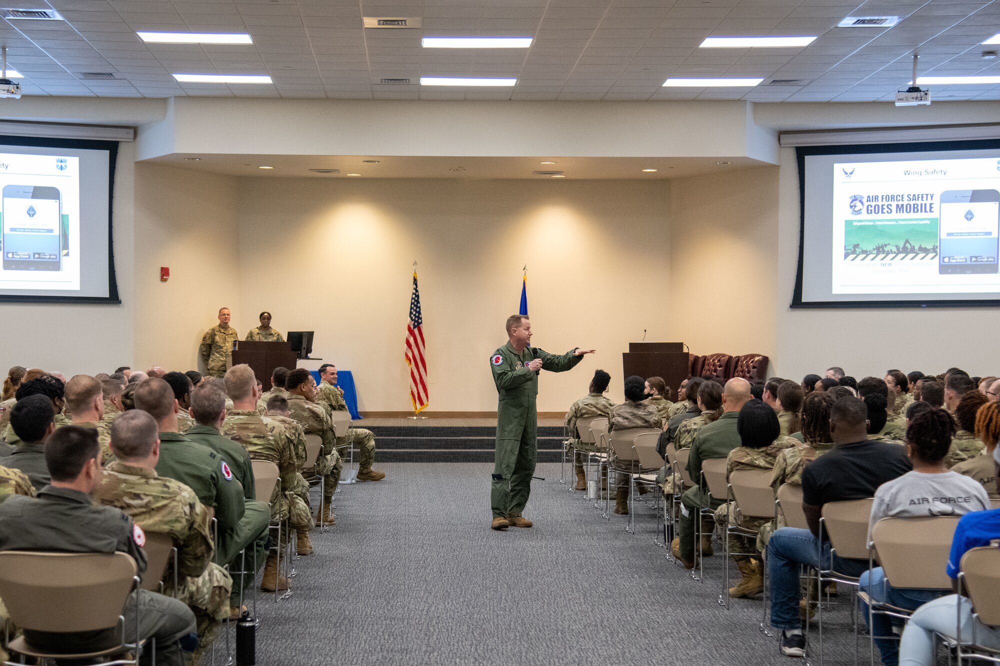 Lt. Col. Cross stands in the middle of an aisle with people sitting on both sides.