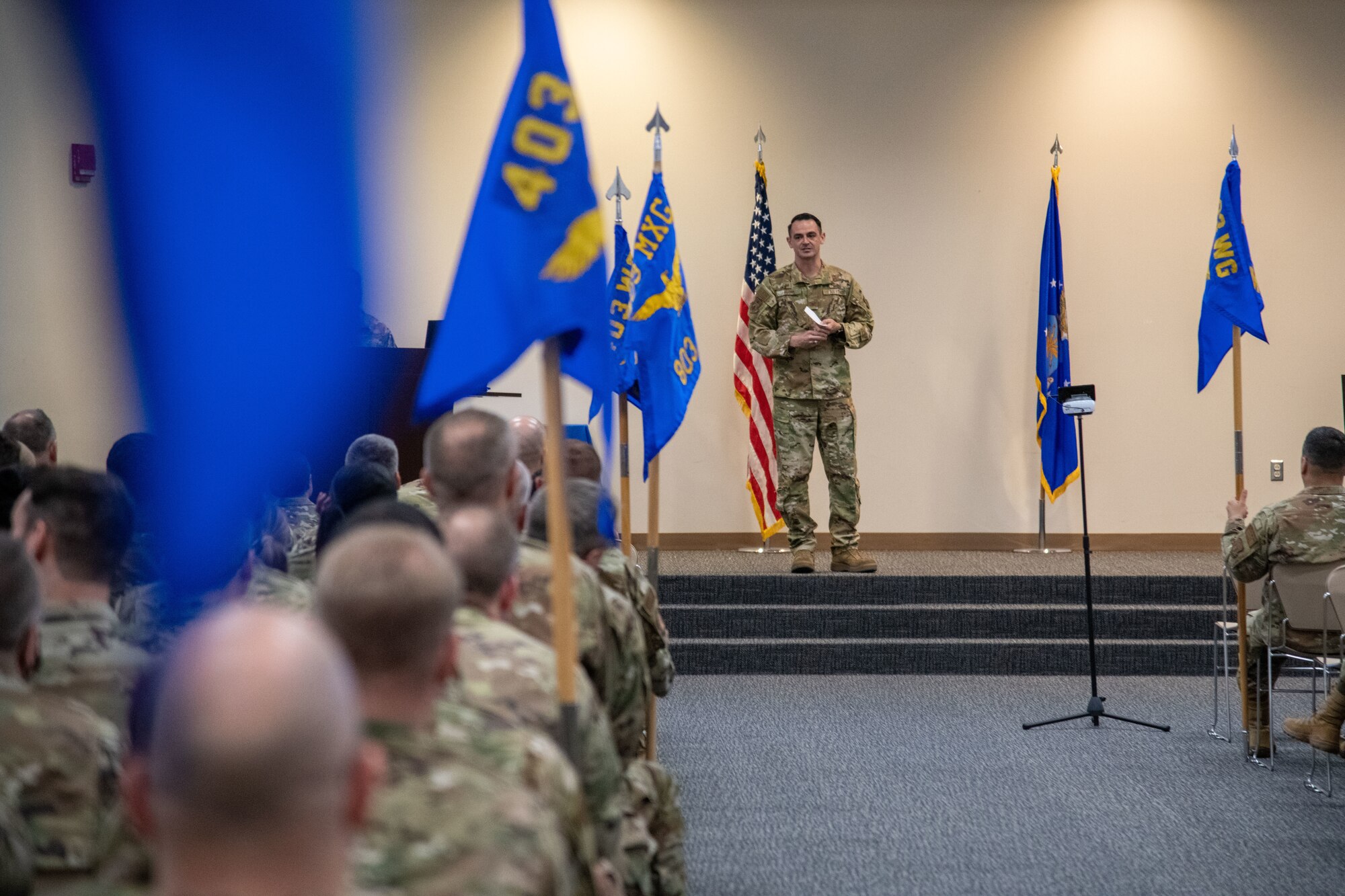 Airmen sit in the foreground as Col. Rubio stands on the stage talking to them