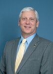 Man with white hair in grey suit and tie.